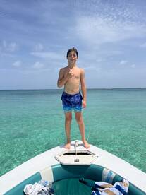 A young boy stands on the bow of a boat, giving a thumbs up against a backdrop of clear turquoise waters — a perfect moment of joy on a boating adventure.