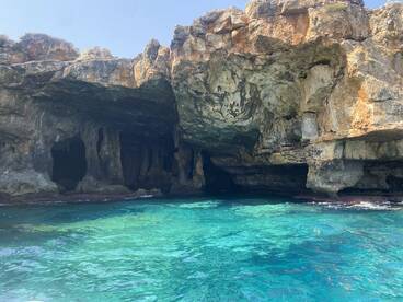 A stunning view of a coastal cave surrounded by crystal-clear turquoise waters, perfect for exploring natural wonders while boating.