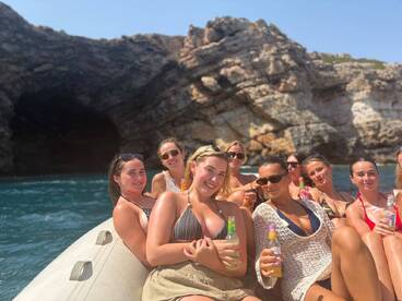 A lively group of friends enjoys drinks on a boat, surrounded by stunning rocky scenery — perfect for a fun day out on the water.