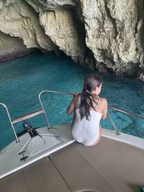 A young girl enjoys the serene beauty of a cave while sitting on the edge of a boat, surrounded by crystal-clear waters — a perfect moment of exploration and adventure.