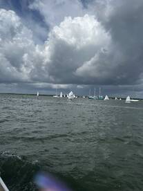 A scenic view of multiple sailboats participating in a regatta under a dramatic sky, showcasing the excitement of sailing on open waters.