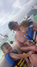 A father enjoys a fun day on the water with his two young children, all wearing life jackets, capturing a joyful family moment aboard a boat.
