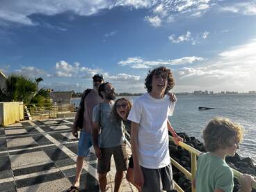 A joyful family poses by the ocean, capturing a fun moment together with a beautiful waterfront backdrop.