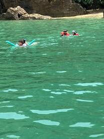 A family enjoys a fun day swimming in crystal-clear waters, with kids using pool noodles and snorkeling gear — a perfect beach adventure.
