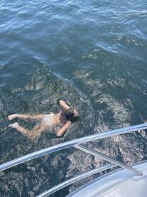 A person enjoys a refreshing swim in the open water, with a boat visible in the foreground — a perfect moment for summer fun on the water.