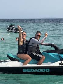 A joyful couple enjoys a thrilling ride on a jet ski in clear waters, surrounded by friends swimming nearby — perfect for adventurous water activities.