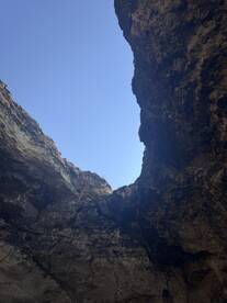 An unclear view of a rocky formation against a bright blue sky, possibly depicting a natural cave or cliff structure.