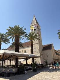 A scenic view of a historic building with palm trees and outdoor seating, capturing the essence of a vibrant coastal town.