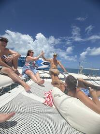 A lively group enjoys a sunny day on a catamaran, sharing laughs and drinks while soaking up the sun — perfect for a fun day at sea.