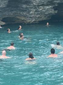 A lively group enjoys swimming in clear turquoise waters near a rocky cave, capturing the essence of adventure and fun in the great outdoors.