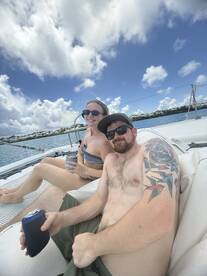 A couple enjoys drinks on the deck of a yacht under a bright sky, capturing the essence of a perfect day on the water.