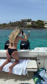 A woman enjoys a sunny day on the water, capturing the moment with her phone while relaxing on the boat — a perfect snapshot of a boating adventure.