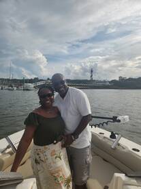 A joyful couple poses together on a boat with a scenic lighthouse in the background, perfect for romantic outings or memorable celebrations on the water.