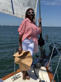 A joyful woman poses on the deck of a sailboat, enjoying a sunny day on the water — perfect for summer sailing adventures.