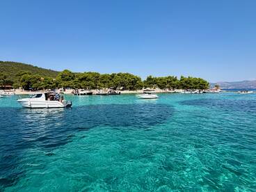 A picturesque view of boats anchored near a beautiful beach with clear turquoise waters, showcasing a perfect summer day on the coast.
