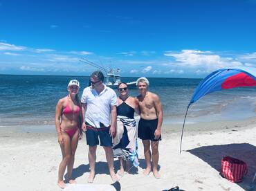 A joyful family poses together on the beach with a boat in the background, capturing a perfect day of sun and fun by the water.