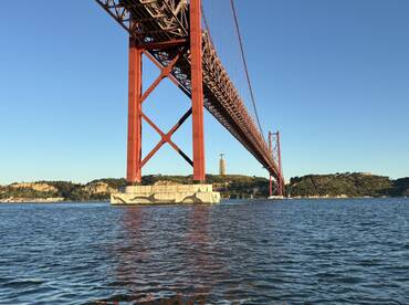 A stunning view of the iconic red bridge spanning over the water, framed by lush hills and clear skies — a perfect representation of the scenic beauty of the area.