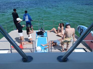 A lively group enjoys a sunny day on a pontoon boat, capturing moments and relaxing on the deck — perfect for summer parties and fun on the water.