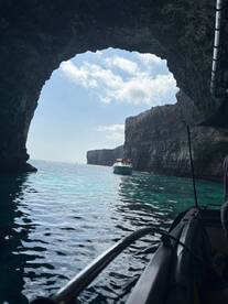 A stunning view of a boat navigating through a natural cave along the coastline, showcasing the beauty of the surrounding waters and cliffs — perfect for adventure seekers exploring hidden gems.