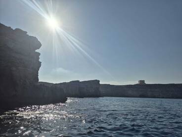 A stunning view of rugged cliffs and sparkling waters under a bright sun, showcasing the natural beauty of the coastline.