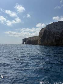 A stunning view of a rocky coastline with a natural arch, captured from the water — perfect for showcasing the beauty of island destinations.