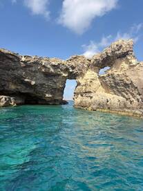 A stunning view of a natural rock arch against a clear blue sky, showcasing the beautiful coastline and turquoise waters — a perfect destination for boating adventures.