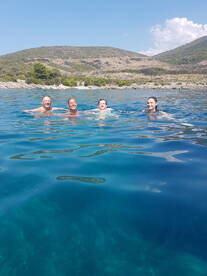 A joyful group swims in the crystal-clear waters near an island, enjoying a refreshing day on the water — perfect for summer adventures.