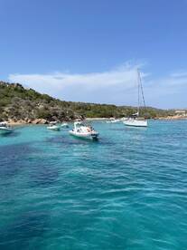 A scenic view of multiple boats anchored in crystal-clear turquoise waters near a beach, showcasing a perfect day for relaxation and water activities.