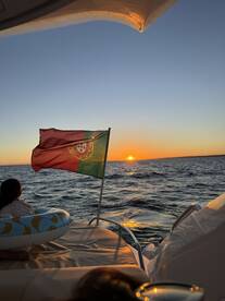 A serene sunset view from a boat, featuring a Portuguese flag and a child enjoying the moment — a perfect scene for family outings on the water.
