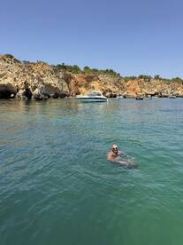 A man enjoys a refreshing swim in clear waters near a picturesque coastline, with a boat anchored nearby — a perfect scene for summer adventures.