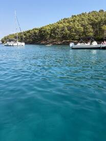 A picturesque view of a sailboat anchored in clear turquoise waters, surrounded by lush greenery — a perfect setting for a relaxing day on the water.