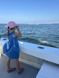 A young girl uses binoculars to explore the ocean from the deck of a boat, capturing the spirit of adventure and discovery on the water.