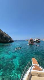 A lively scene of people swimming in crystal-clear waters, with several boats anchored nearby, perfect for a fun day out on the water.