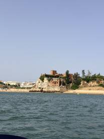 A picturesque view of a historic castle perched on a cliff, overlooking a beautiful beach — a stunning coastal landmark perfect for sightseeing during boat tours.