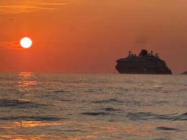 A stunning sunset casts a warm glow over a cruise ship silhouetted against the horizon, creating a picturesque maritime scene.