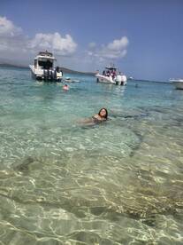 A woman enjoys swimming in crystal-clear waters while boats are anchored nearby, capturing the essence of a perfect beach day.