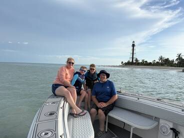 A joyful family poses on their boat with a scenic lighthouse in the background, capturing a memorable day on the water.
