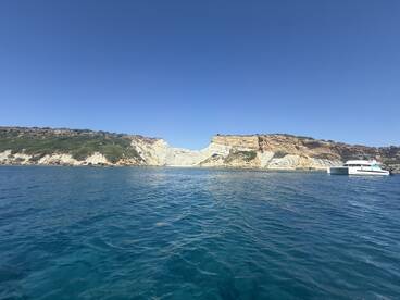 A stunning view of a catamaran anchored near a picturesque coastline, showcasing the beautiful cliffs and clear blue waters — perfect for island exploration and scenic boat trips.