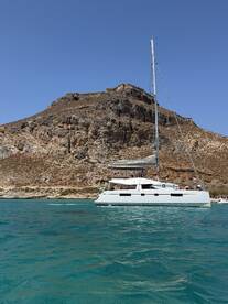 A sleek catamaran sails in clear turquoise waters, set against a stunning rocky backdrop — perfect for exploring coastal destinations.