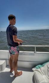 A young adult enjoys a day of fishing on a boat, casting a line into the open ocean under a clear blue sky.