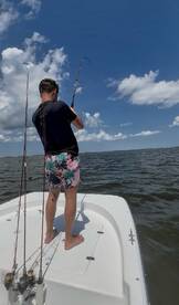 A young man enjoys a fishing adventure on a boat, showcasing the thrill of reeling in a catch under a bright blue sky.