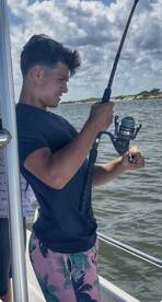 A young man focuses intently while fishing from a boat, showcasing the excitement of on-water activities. Perfect for fishing enthusiasts and adventure seekers.