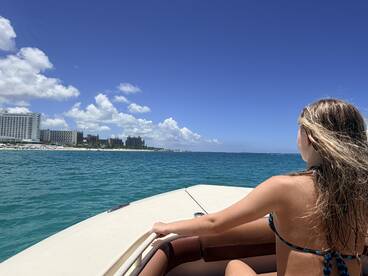 A young girl enjoys the ocean view from the boat, with a stunning backdrop of hotels and a clear blue sky — a perfect moment capturing the essence of a tropical getaway.