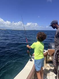 A child enjoys fishing on a boat, guided by an adult, surrounded by the beautiful ocean — a perfect family adventure on the water.