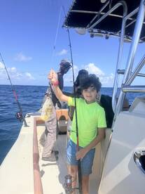 A young boy proudly holds up his catch while fishing on a boat, surrounded by friends — a perfect moment of joy on the water.