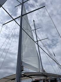 A close-up view of the mast and sail of a sailboat against a cloudy sky, showcasing the intricate rigging and design typical of sailing vessels.
