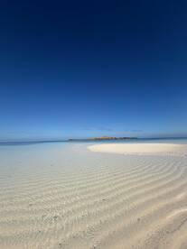 A stunning view of a serene beach with crystal-clear waters and a distant island, perfect for showcasing tropical destinations and tranquil getaways.