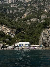 A scenic view of a beach with a charming building and guests enjoying the sun, surrounded by stunning cliffs — a perfect destination for relaxation and exploration.