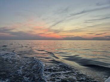 A serene sunset over calm ocean waters, showcasing beautiful hues reflecting on the surface — perfect for capturing the tranquility of a boating experience.
