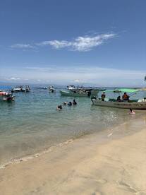 A lively scene at the beach with groups enjoying snorkeling and swimming, surrounded by boats offering fishing and snorkeling tours — a perfect day for water activities.